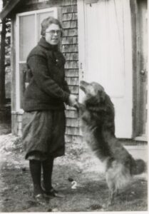 Leona Cadorette pictured in middle age, standing in front of a house with a golden retriever dog. 